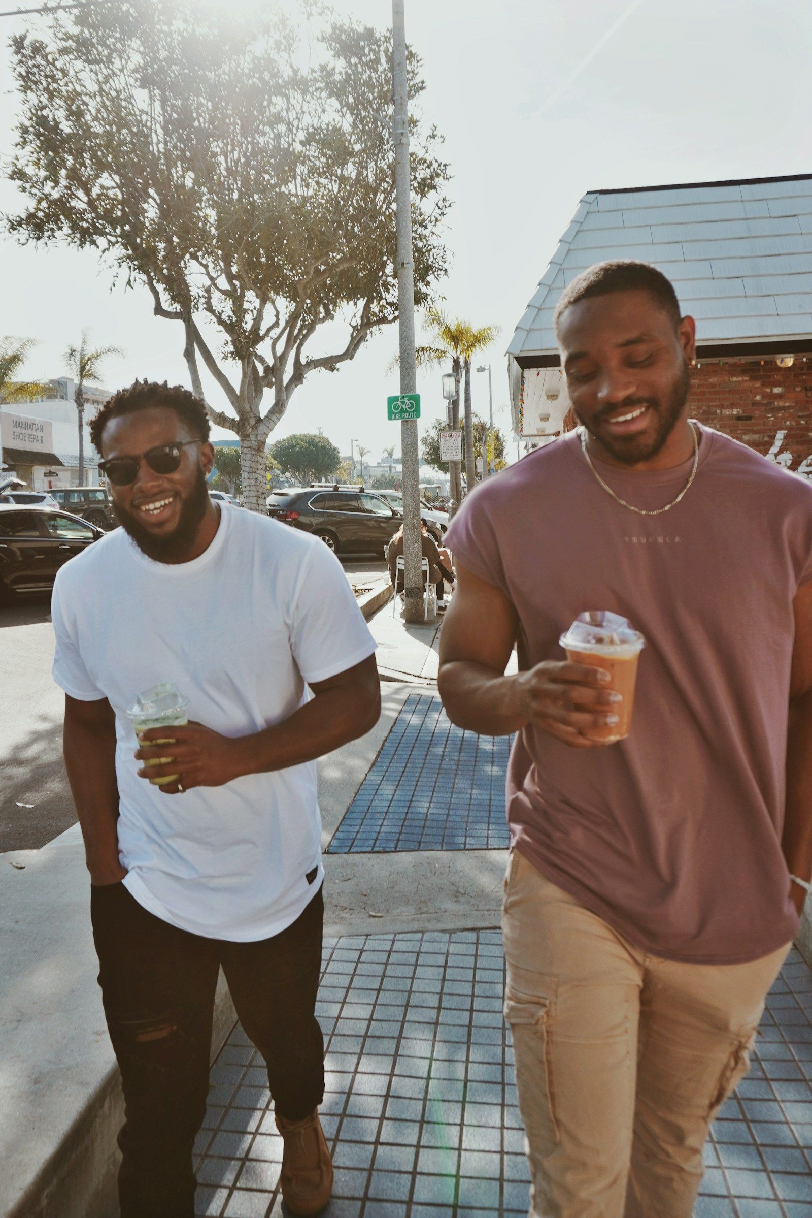 Two men laughing as they walk with iced coffees